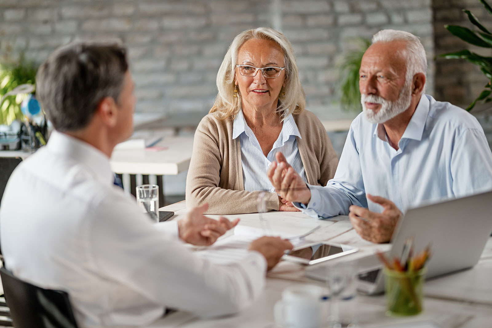 Senior Couple Sitting on couch facing insurance agent writing on clipboard