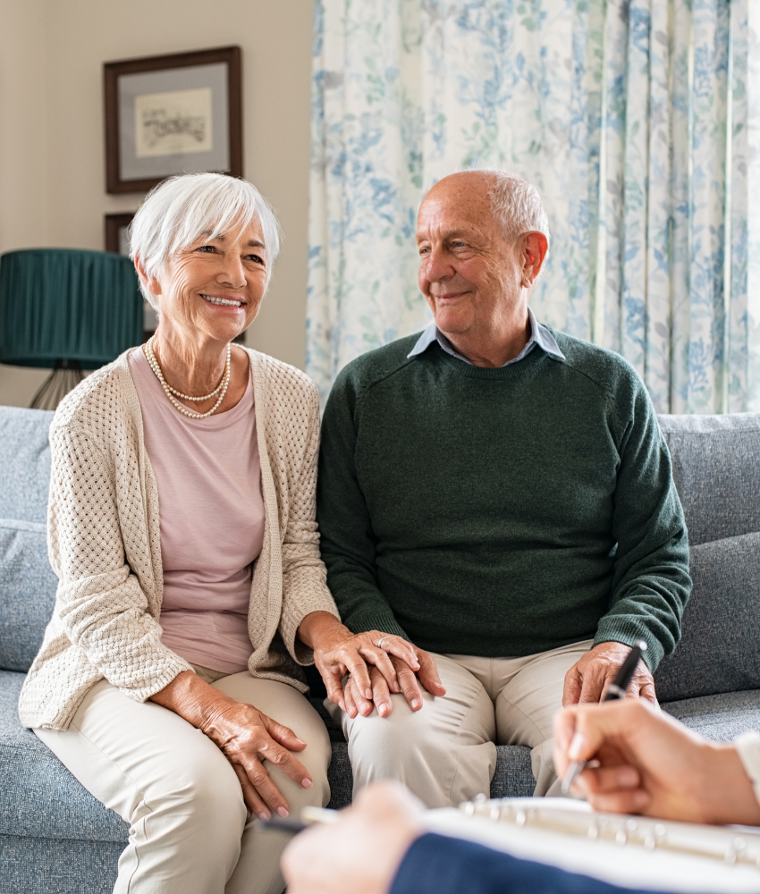 Senior Couple Sitting on couch facing insurance agent writing on clipboard